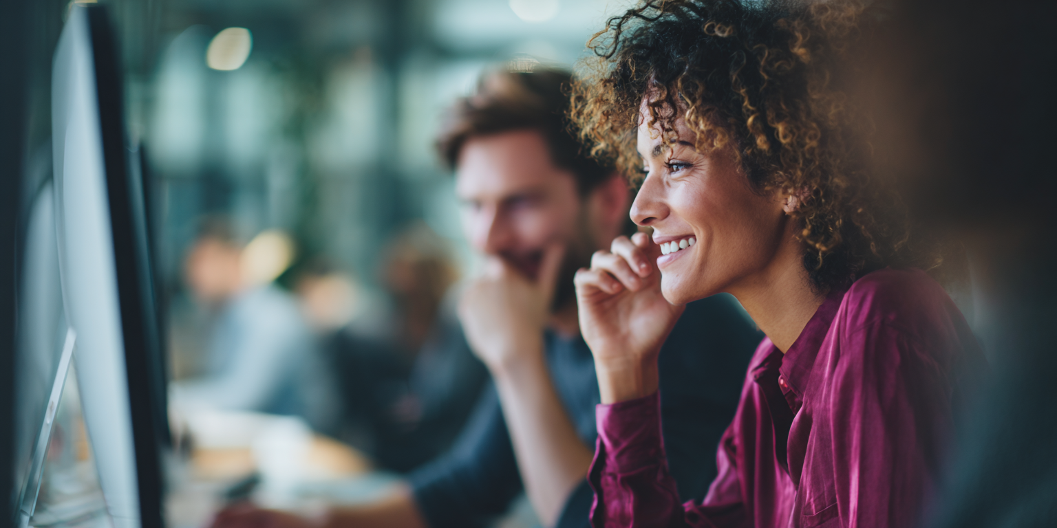 Smiling woman and man collaborating at a computer in a modern office environment.