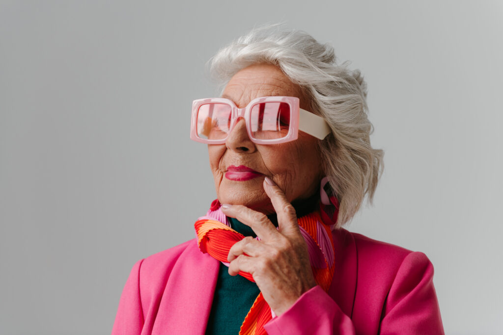 Pension Elegant elderly woman wearing fashionable retro styled eyeglasses and radiating self-love on grey background